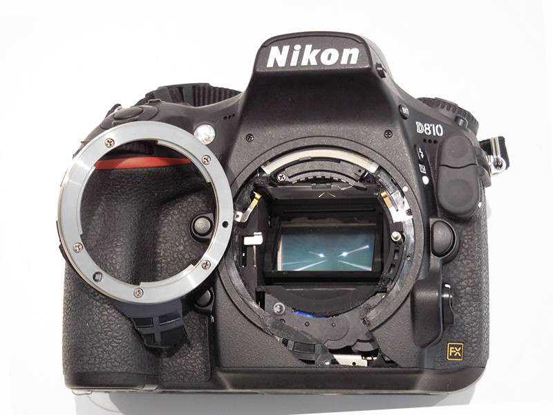 Nikon D810 de face avec la bague de monture complètement arrachée et séparée du boîtier, exposant le capteur et les composants internes