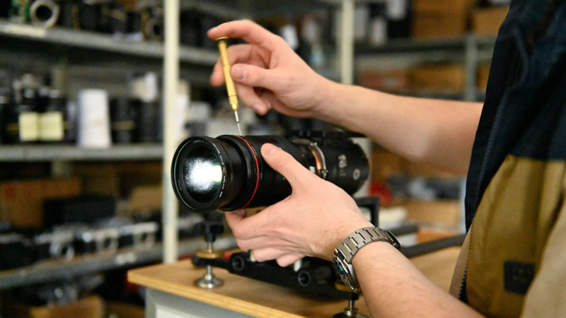 Technicien manipulant un objectif Canon rouge avec un tournevis de précision dans un atelier de réparation photo, pour diagnostiquer une erreur Err 01