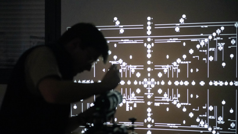 Technicien de réparation photo travaillant sous un schéma électronique projeté sur grand écran dans un atelier sombre
