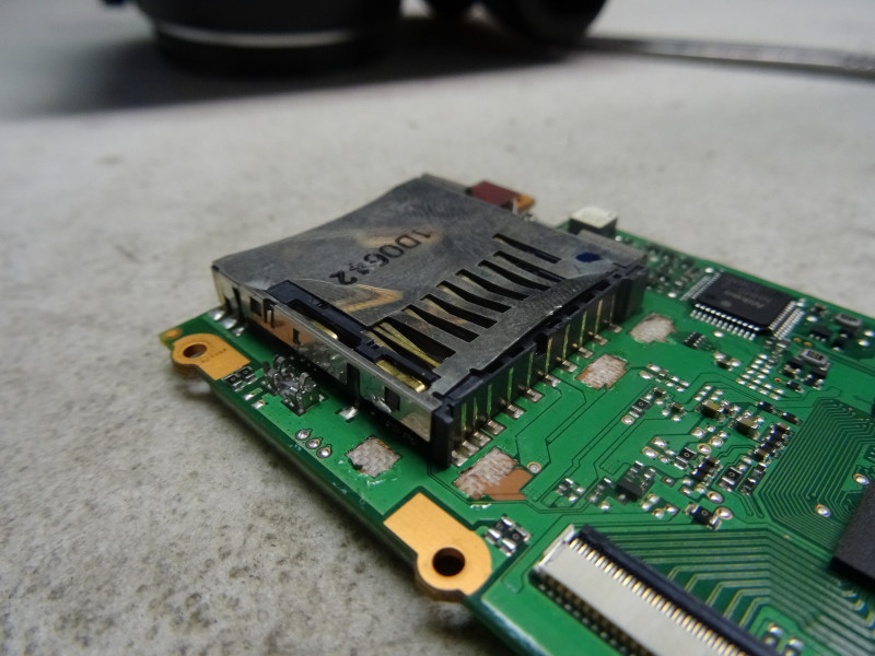 Gros plan sur un slot de carte SD monté sur une carte électronique verte d'appareil photo, montrant les contacts et le mécanisme de verrouillage